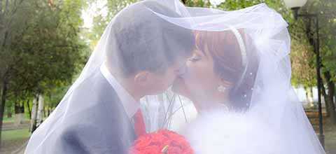 Bride and groom kissing under wedding veil.